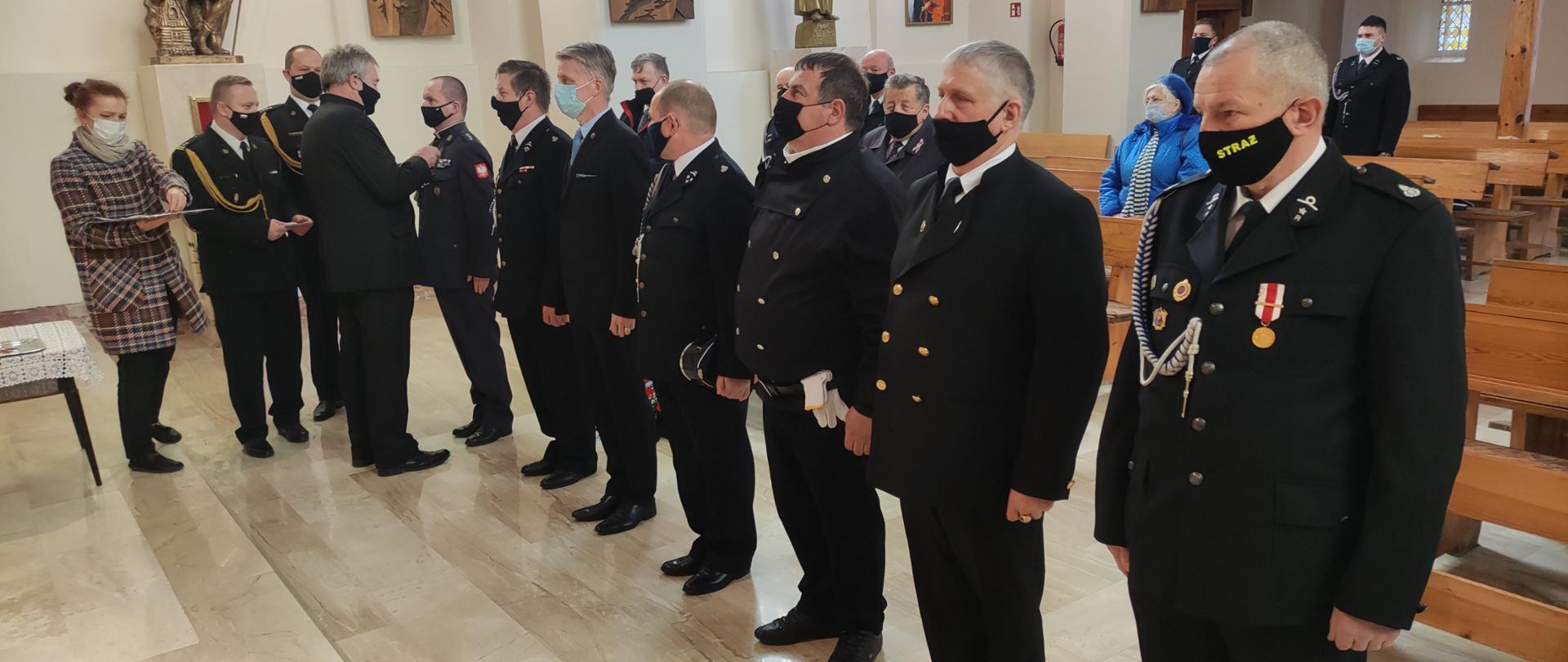 Odznaczeni stoją w szeregu a naprzeciw nich osoby, które przypinają i gratulują.