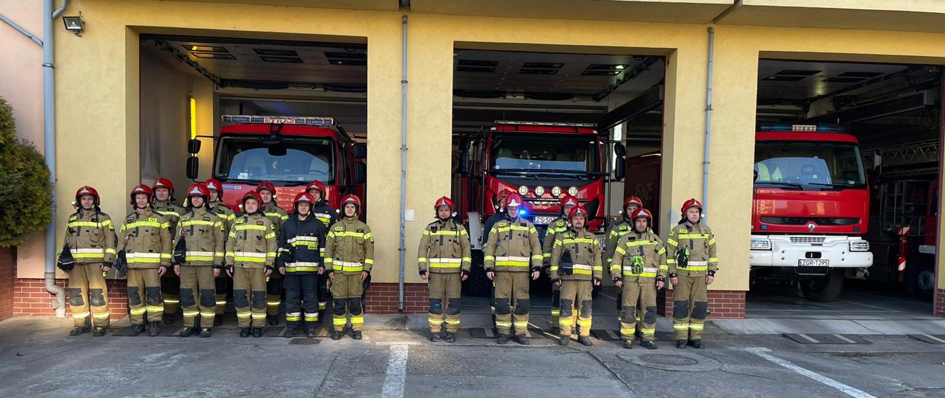 Zdjęcie zrobione na tle Komendy Powiatowej Państwowej Straży Pożarnej w Gryfinie. Na zdjęciu strażacy zmiany zdającej i przyjmującej stoją na baczność w szeregu. D