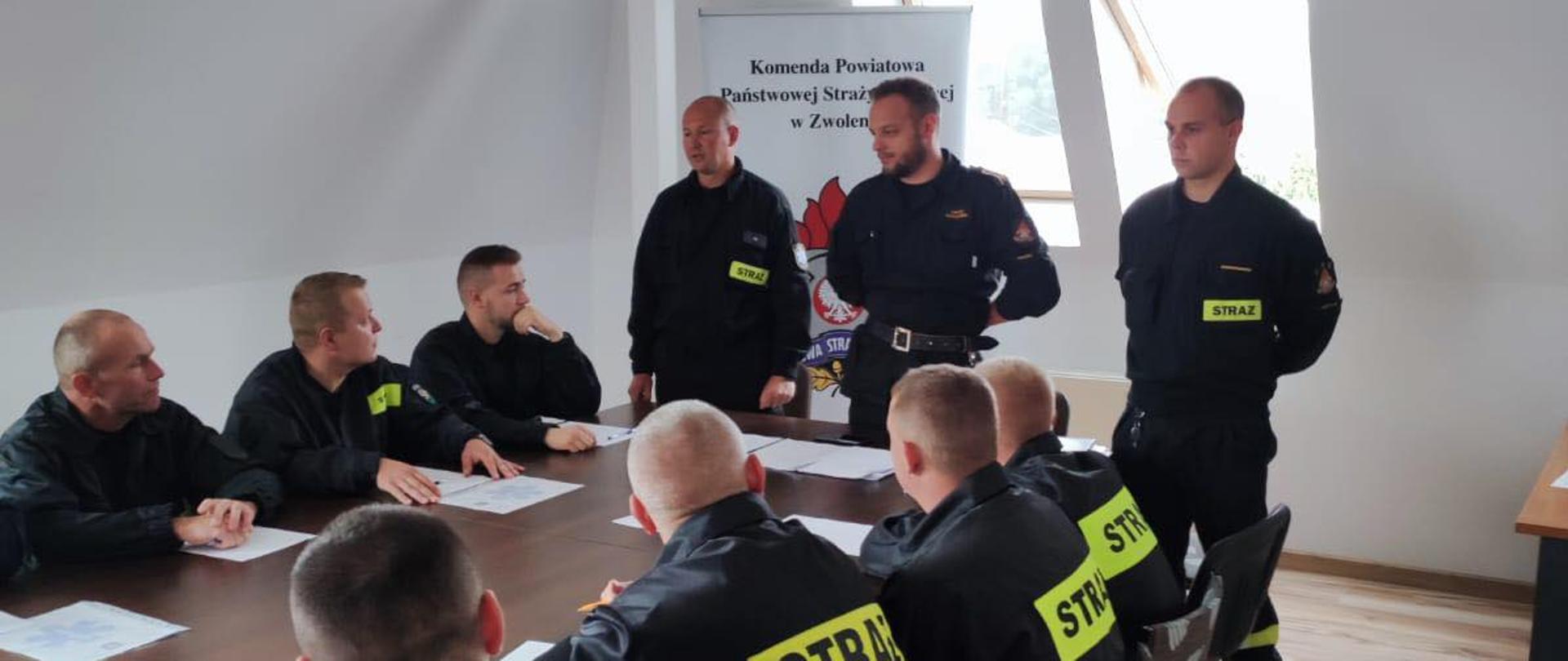 Egzamin, uczestnicy siedzą przy biurkach, w tle komisja egzaminacyjna