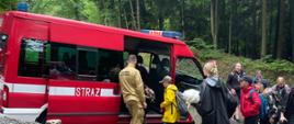 Na zdjęciu widać samochód Państwowej Straży Pożarnej do, którego wsiada grupa harcerzy. Przy samochodzie stoi również strażak oparty na karoserie pojazdu. W tle można zobaczyć drzewa.