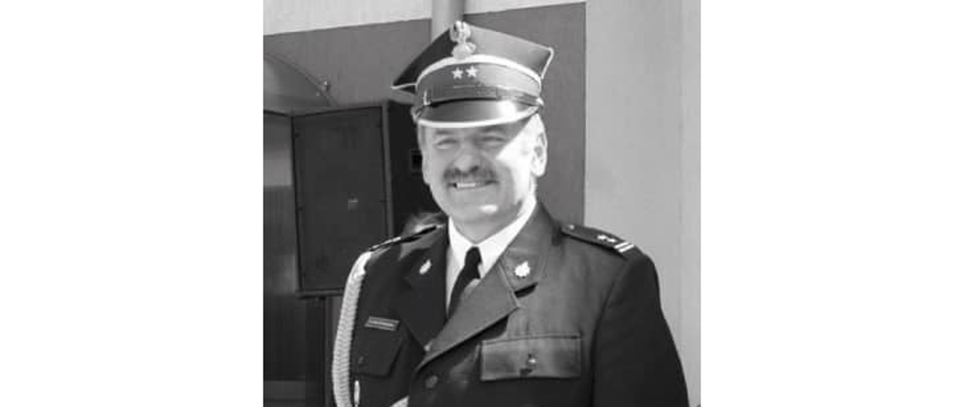 czarno białe zdjęcie strażaka w mundurze ze sznurem i w rogatywce, strażak się uśmiecha