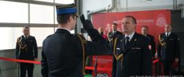 Zdjęcie przedstawia dowódcę uroczystości salutującemu Komendantowi Powiatowemu PSP st. bryg. Bogusławowi Goleni. W tle widać innych funkcjonariuszy, którzy prowadzą uroczystość przejścia na zaopatrzenie emerytalne dwóch strażaków.