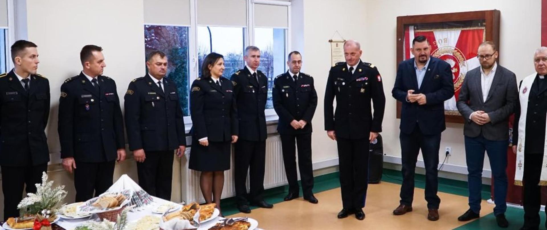 Zdjęcie przedstawia spotkanie wigilijne zorganizowane na świetlicy KP. Na środku przybrany stół, w drugim planie strażacy biorący udział w spotkaniu.