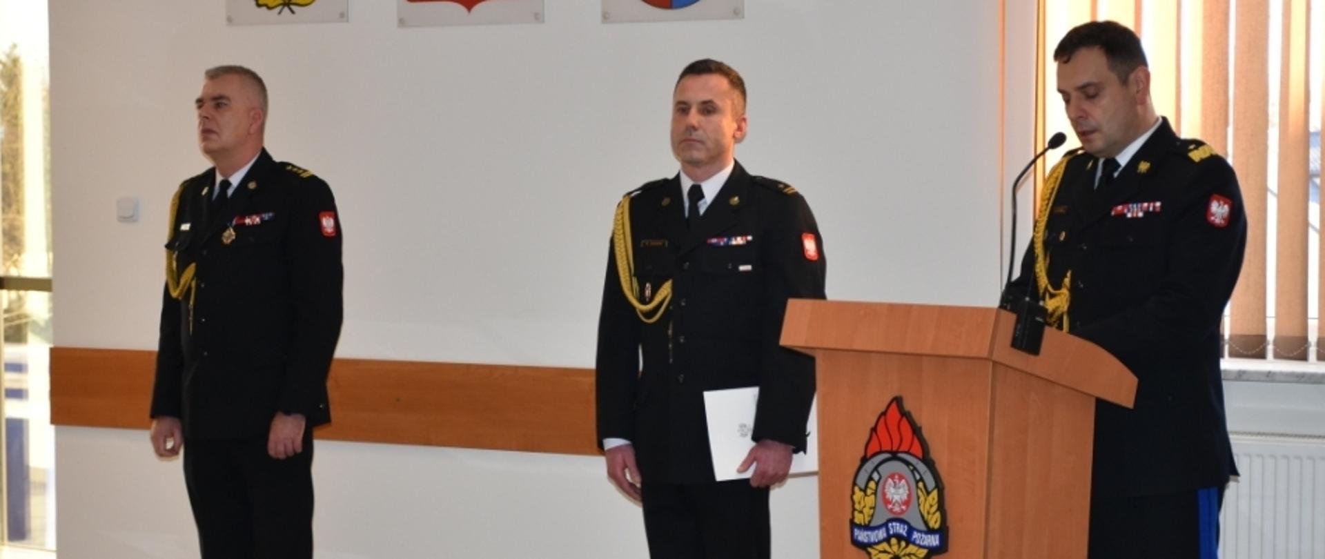 Komendant wojewódzki PSP w Kielcach przemawia, przedstawiając sylwetkę nowo powołanego komendanta powiatowego PSP w Skarżysku-Kamiennej. Po jego prawej stronie stoi nowo powołany komendant powiatowy, a dalej zastępca komendanta wojewódzkiego PSP.