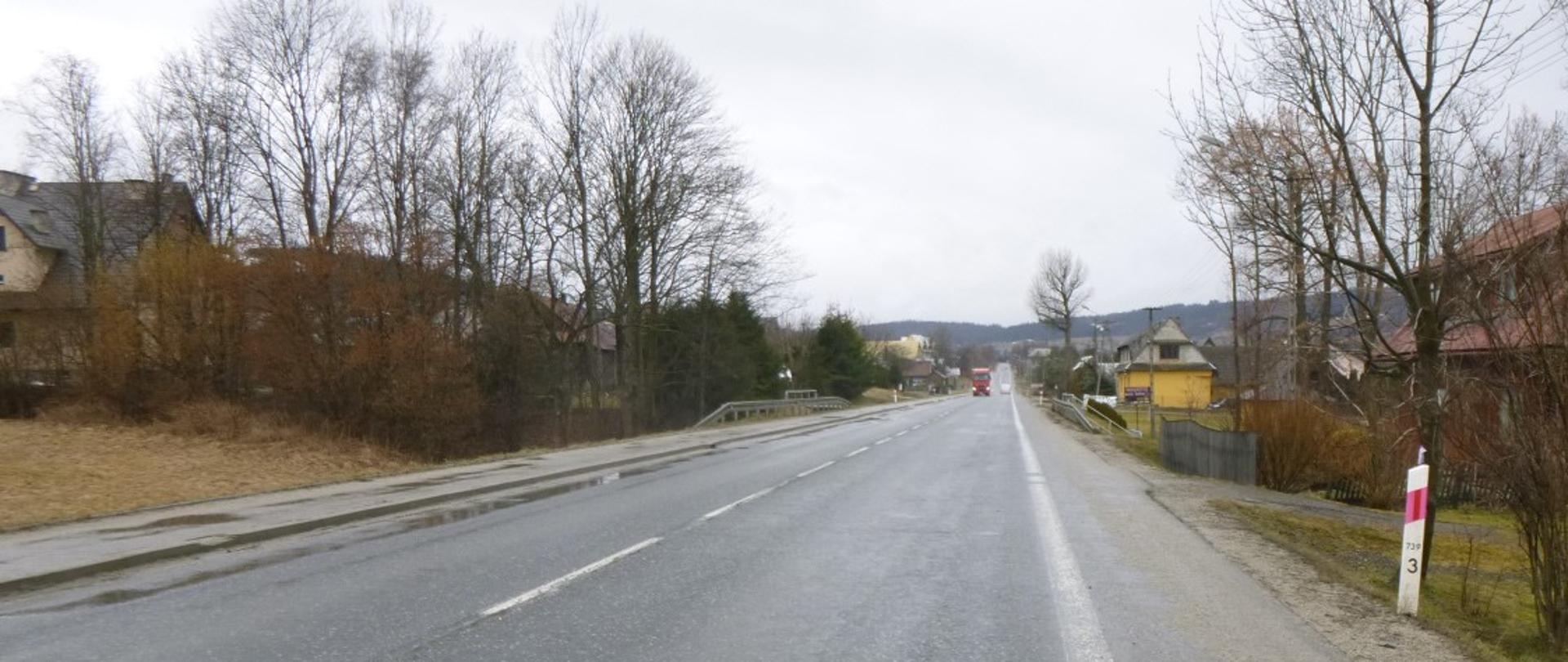 Jezdnia jednopasmowa po jednym pasie ruchu w każdym kierunku. Po prawej stronie widoczne pobocze a po lewej stronie chodnik.