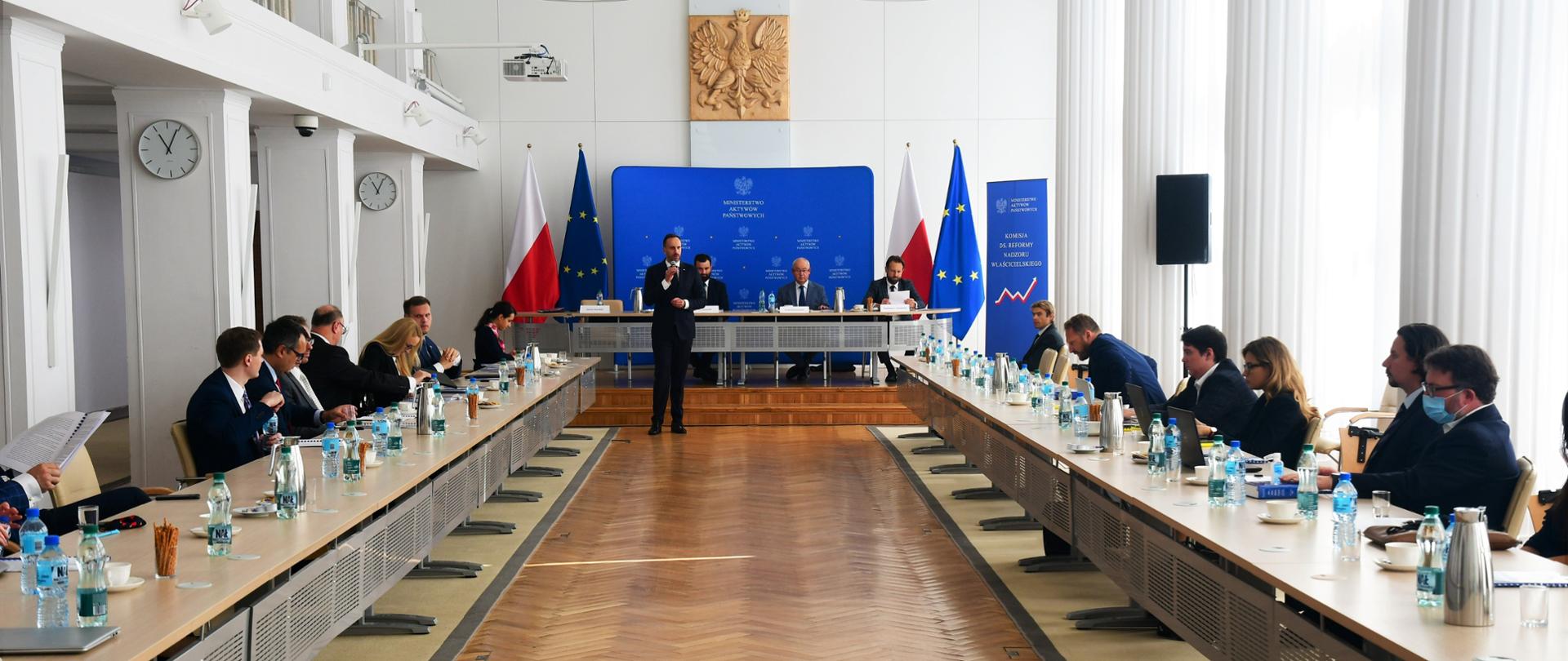 Spotkanie konsultacyjne z udziałem wiceministra Janusza Kowalskiego. Wiceminister przemawia do mikrofonu. Przy stolikach wokół siedzą zaproszeni goście. W tle ścianka MAP.