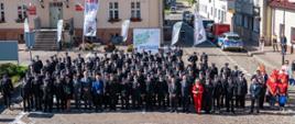 Zdjęcie grupowe zaproszonych gości, druhów OSP oraz komendantów woj. zachodniopomorskiego. W tle budynki Maszewskiego centrum, flagi i banery.