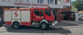 Czerwono biały duży samochód strażacki stoi bokiem/ na drzwiach biały numer 501 E 21 Stoi na zewnątrz przed budynkiem Komendy Powiatowej Państwowej Straży Pożarnej w Poddębicach 