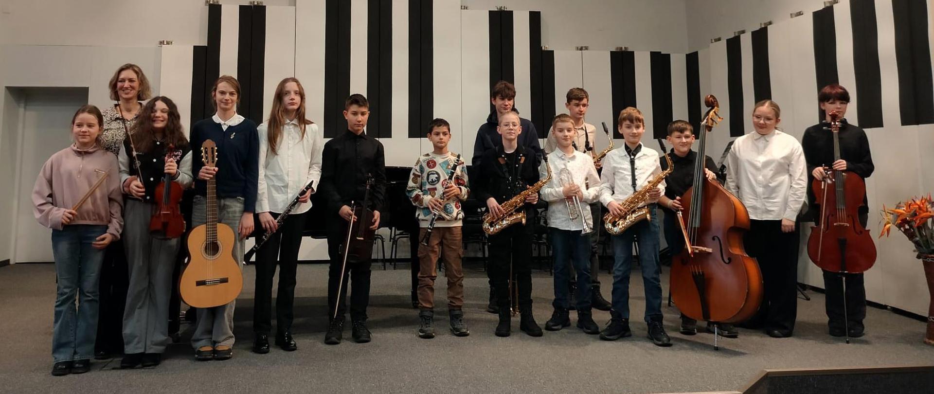 Wszyscy wykonawcy stoją na scenie ze swoimi instrumentami i z nauczycielką.