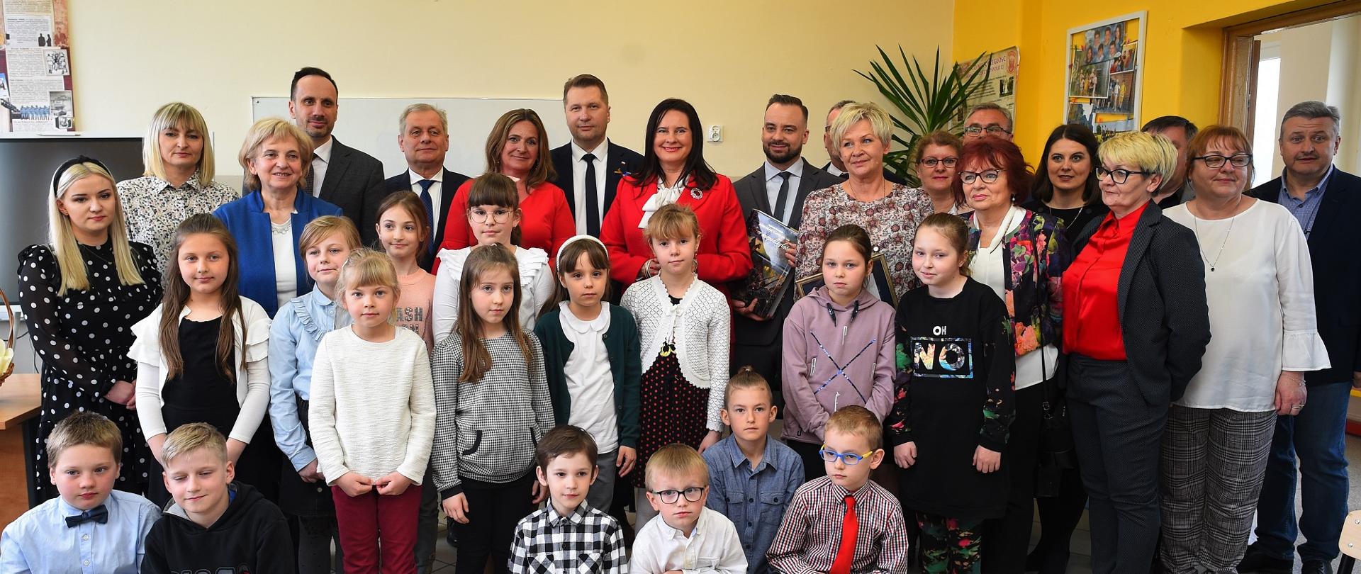 Wizyta w Smarchowicach. Minister stoi w otoczeniu uczniów i nauczycieli.