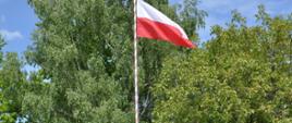 Flaga Rzeczpospolitej powiewa na szczycie masztu flagowego, pod masztem poczet flagowy stoi na baczność