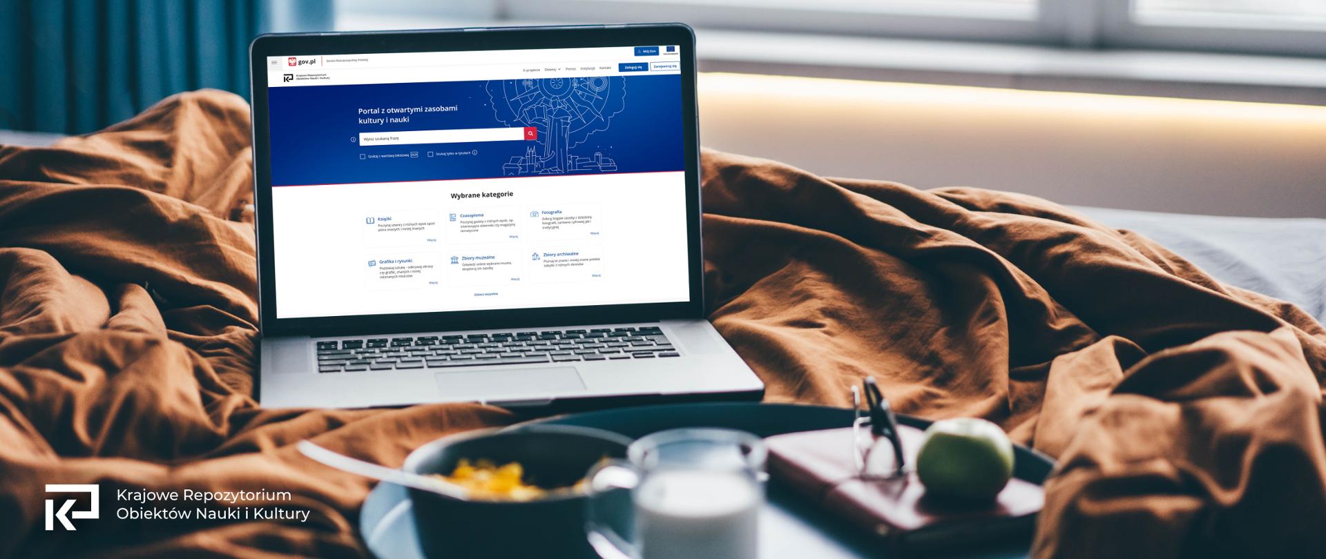 na zdjęciu fragment łóżka, wdać tacę ze śniadaniem, na łóżku włączony laptop a na nim widoczna strona kronika.gov.pl