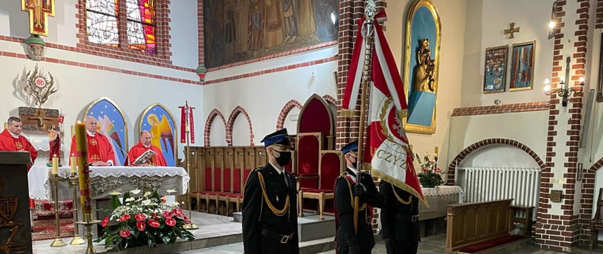 Poczet sztandarowy podczas w wyjścia z kościoła. Sztandar podniesiony na tle ołtarza, na ołtarzu księża celebrujący mszę.