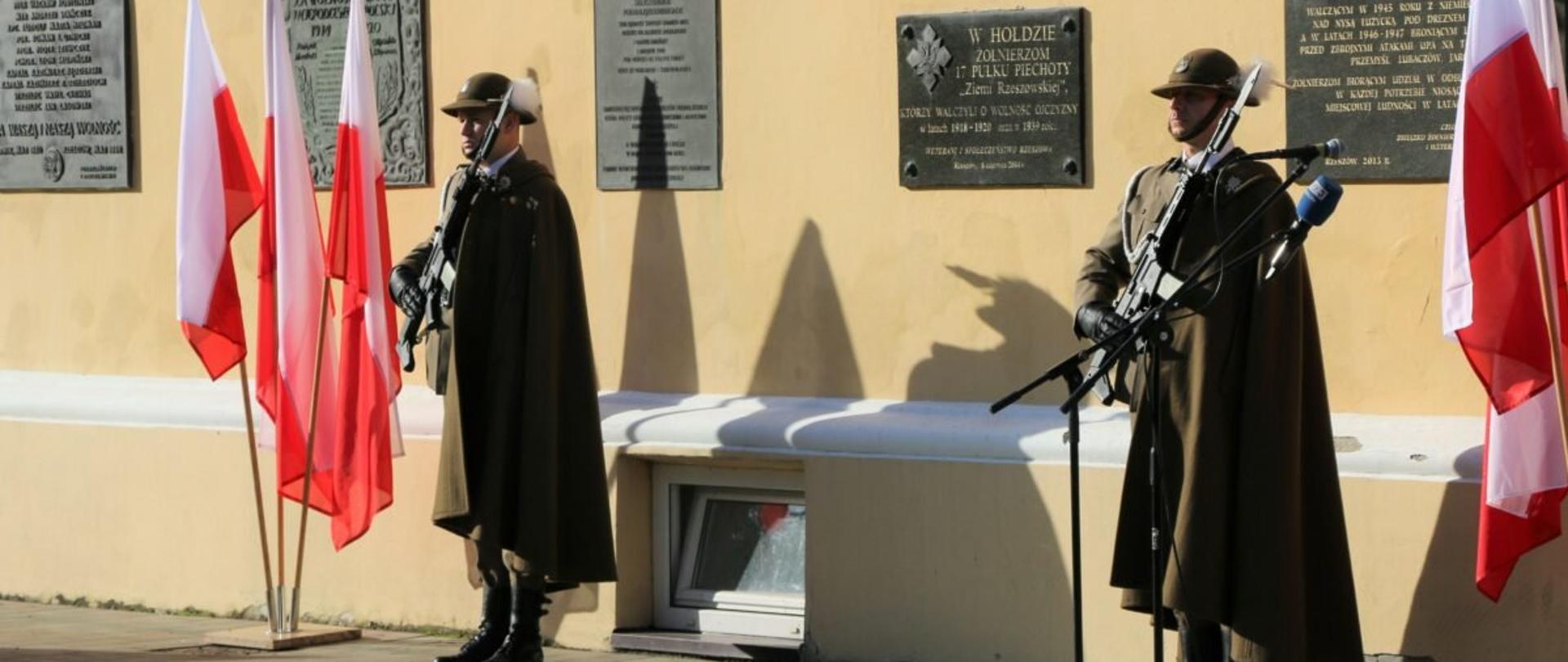 Dwóch żołnierzy stojących przy tablicach pamiętnikowych na murach kościoła