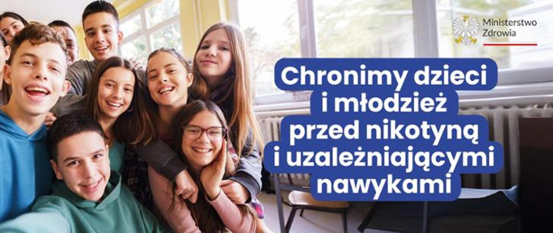 grupa uśmiechniętej młodzieży w sali lekcyjnej, napis chronimy dzieci i młodzież przed nikotyną i uzależniającymi nawykami
