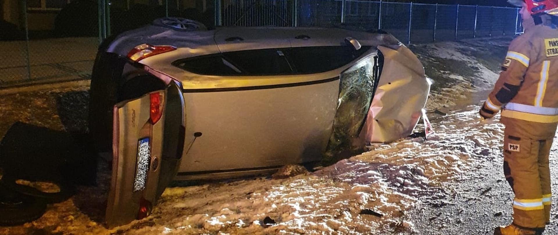 Samochód osobowy koloru srebrnego leży w rowie na prawym boku