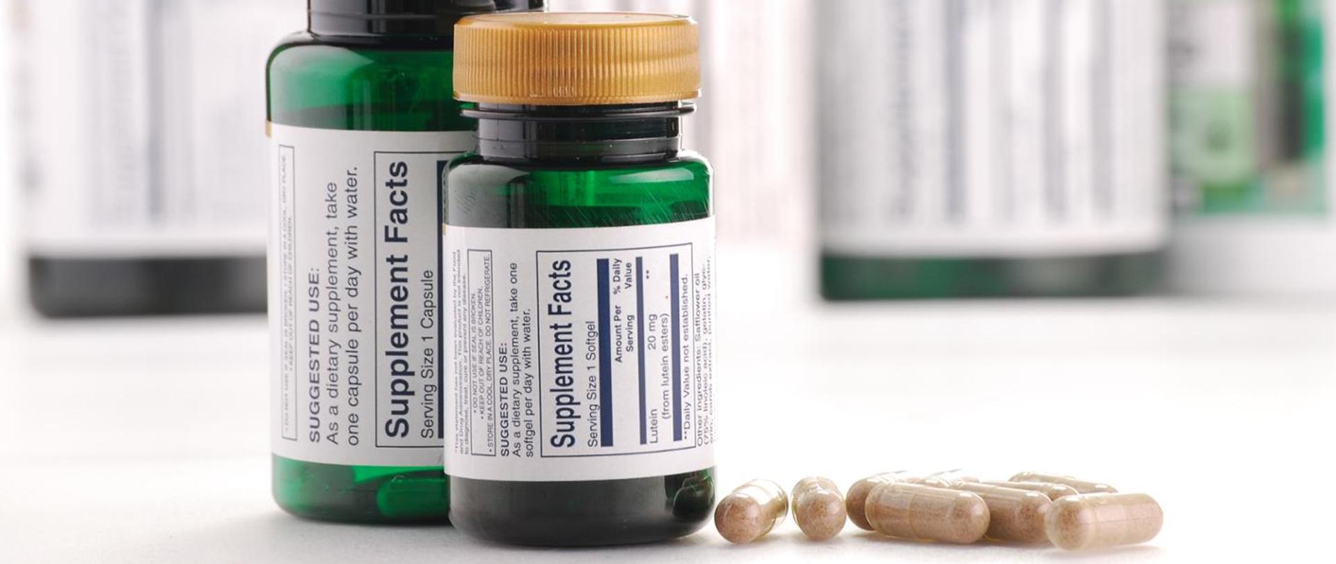 na zdjęciu widać dwie zielone plastikowe buteleczki z suplementami, obok buteleczek leży kilka brązowych kapsułek 