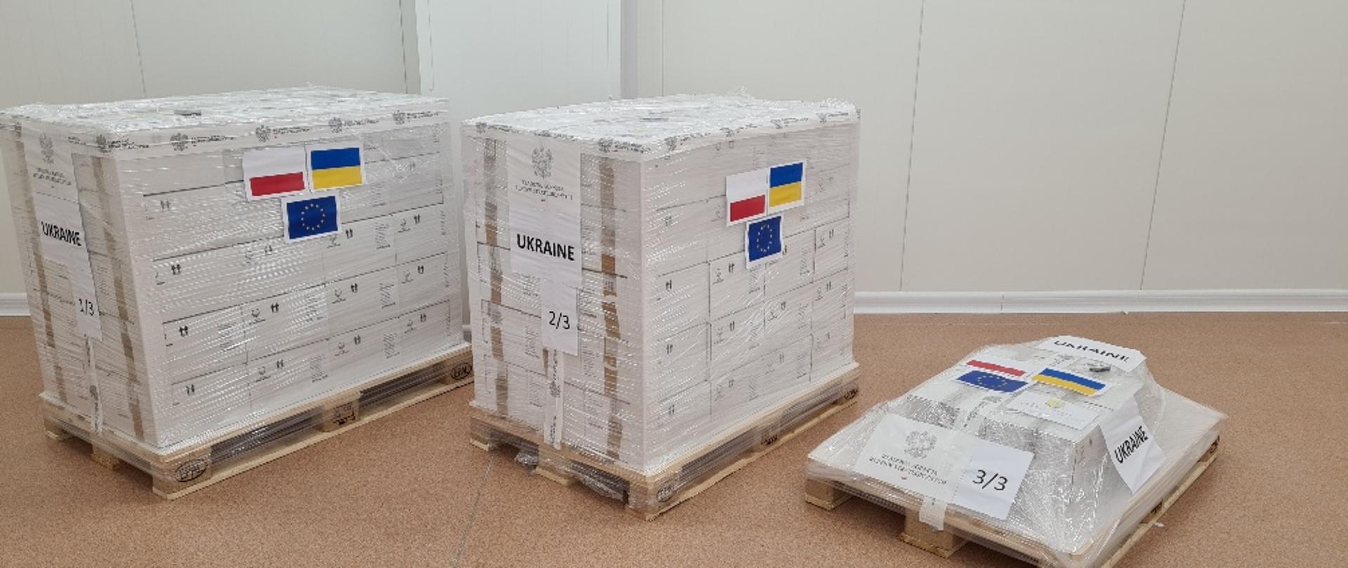 Zafoliowane paczki na paletach z przyklejonymi flagami Polski, Ukrainy i Unii Europejskiej