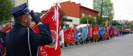 Po lewej stronie tyłem widoczny dowódca pocztów sztandarowych, który salutuje. W centrum i po prawej stronie poczty OSP z pochylonymi sztandarami.