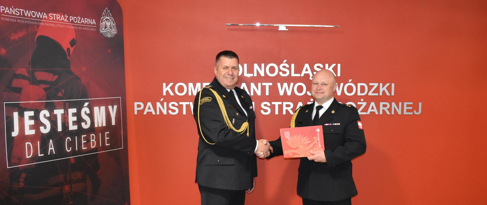 Funkcjonariusze pozując do zdjęcia na tle czerwonej ściany.