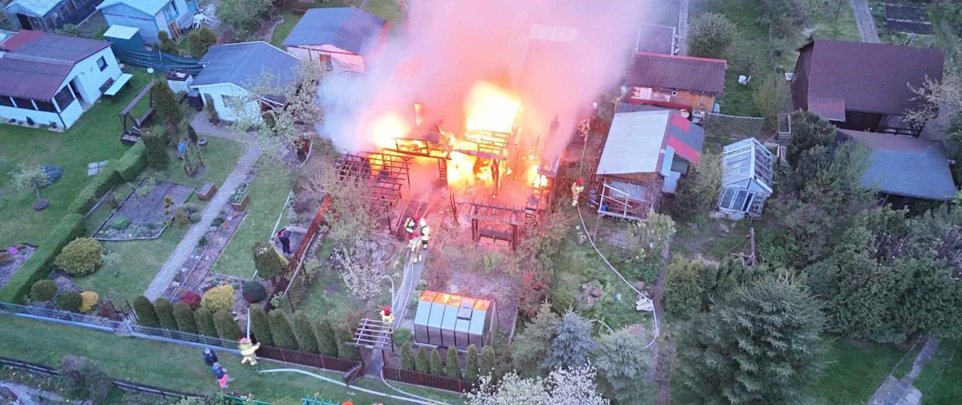 Widok z drona na palącą się altanę oraz akcję gaśniczą strażaków.