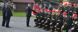 Dzień Strażaka w Sobiałkowie. Na placu przed remizą OSP trwa pasowanie na strażaka-członka MDP., którego dokonuje zastępca komendanta powiatowego PSP. Pasowani klęczą na wężu na prawym kolanie. Obok stoi poczet sztandarowy. 