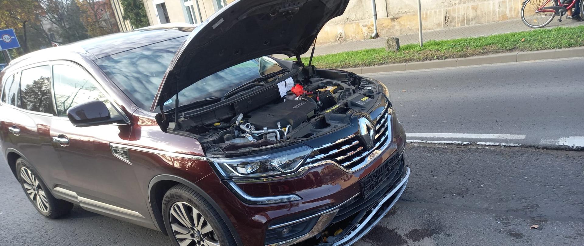 Widać bordowy uszkodzony samochód osobowy od przodu, podniesiona maska