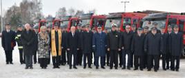 Strażacy oraz zaproszeni goście stoją obok siebie za nimi ustawione są samochody gaśnicze.