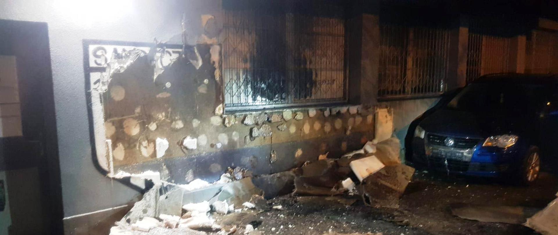 Uszkodzona elewacja budynku oraz samochód osobowy.