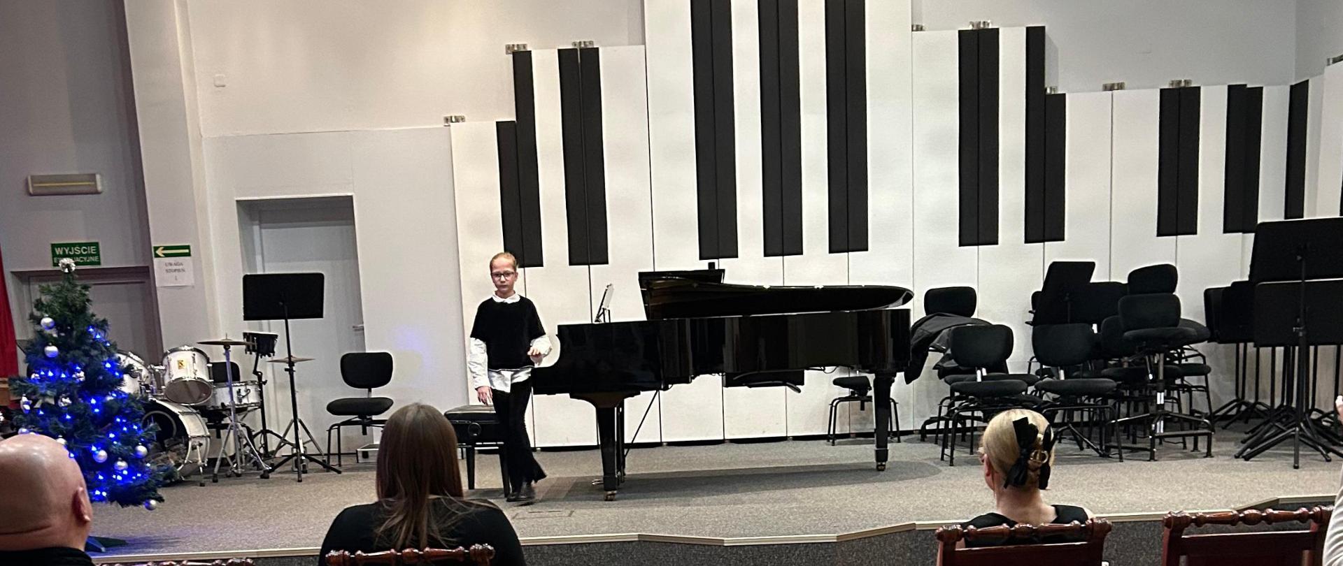 Dziewczyna stoi przy fortepianie.