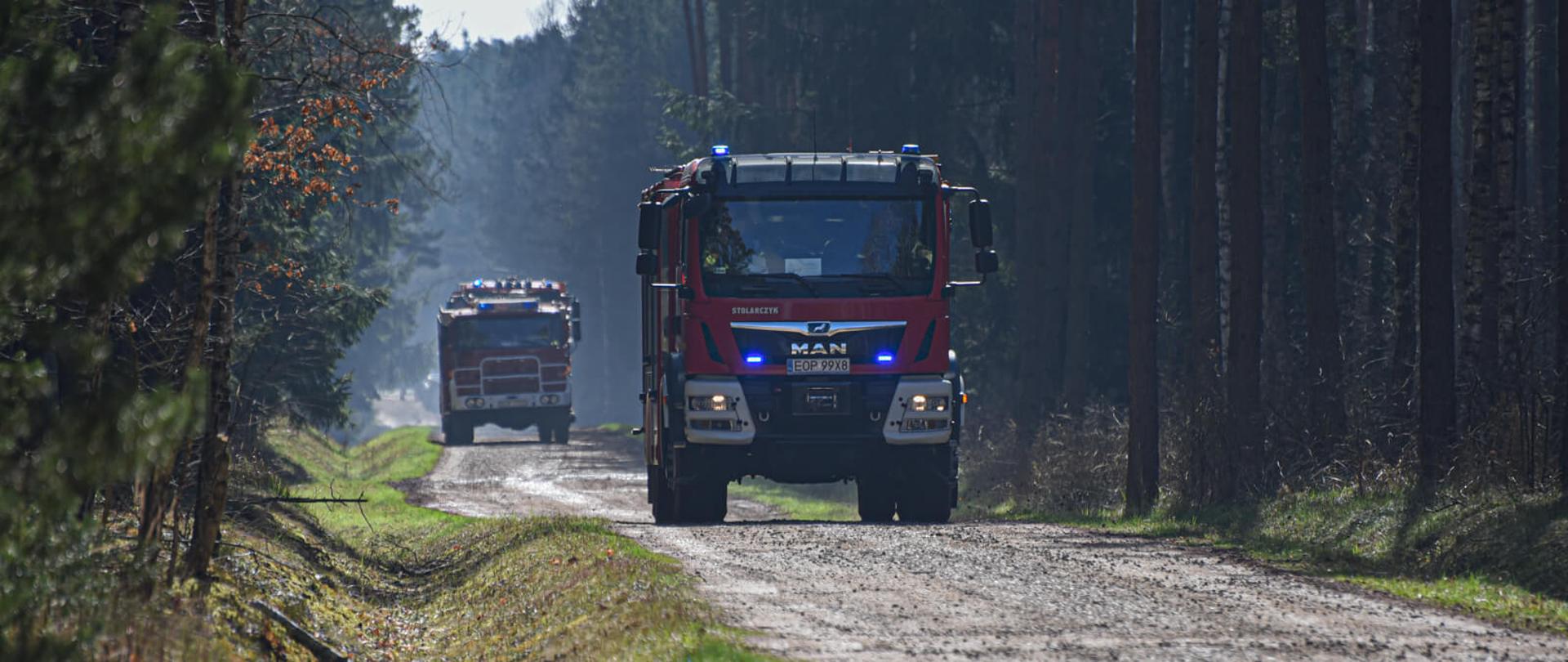 dwa samochody gaśnicze jadą szeroką leśną drogą