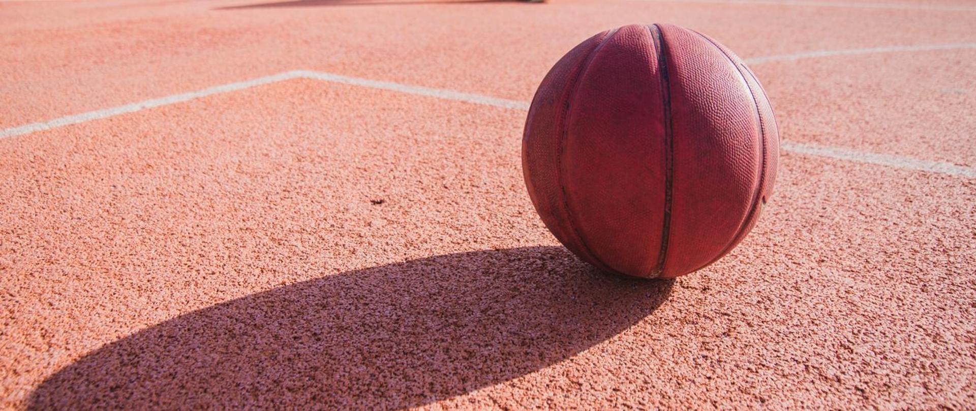 zdjęcie przedstawia podłoże boiska sportowego oraz piłkę do koszykówki