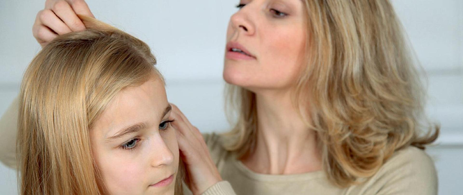 na zdjęciu dorosła kobieta przegląda włosy dziewczynki celem sprawdzenia czy nie ma wszy
