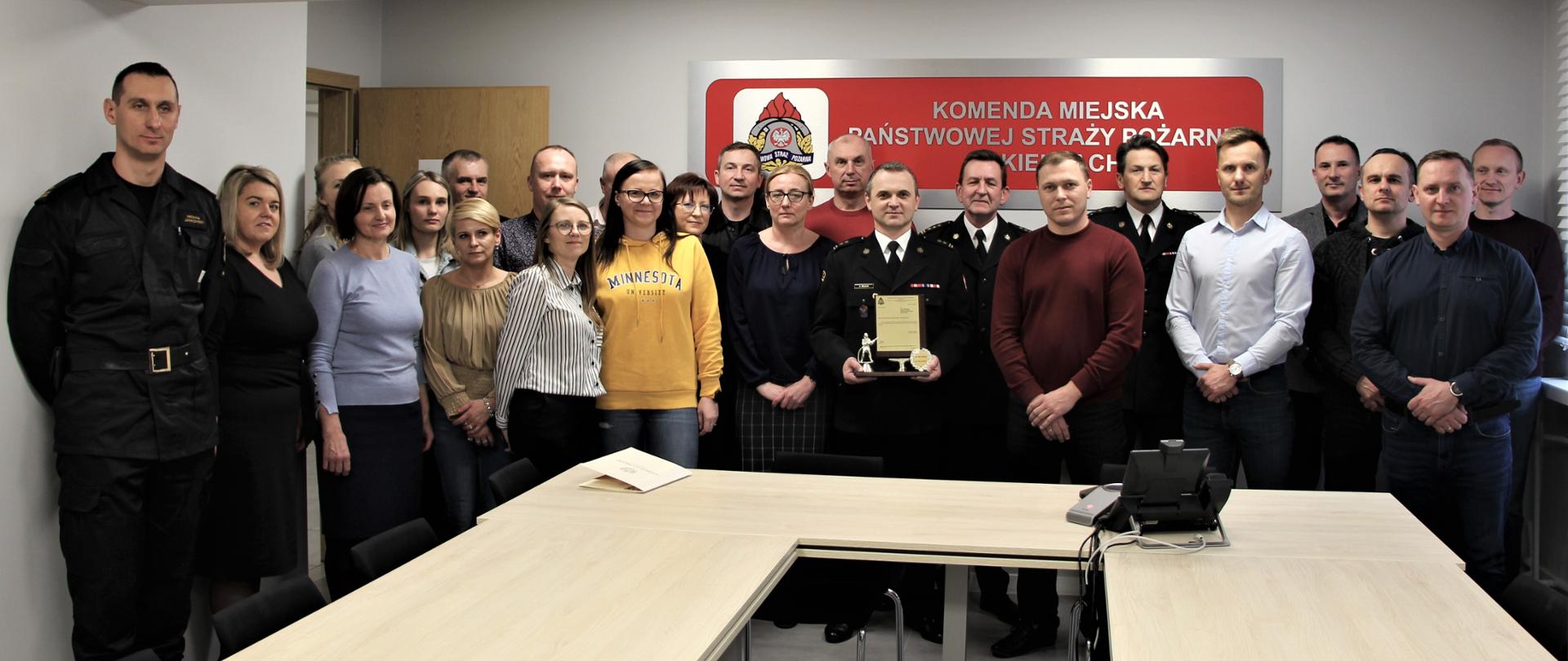 Na zdjęciu przedstawiono zgromadzonych współpracowników odchodzącego naczelnika Wydziału Organizacyjno-Kadrowego z komendy miejskiej Państwowej Straży Pożarnej w Kielcach.