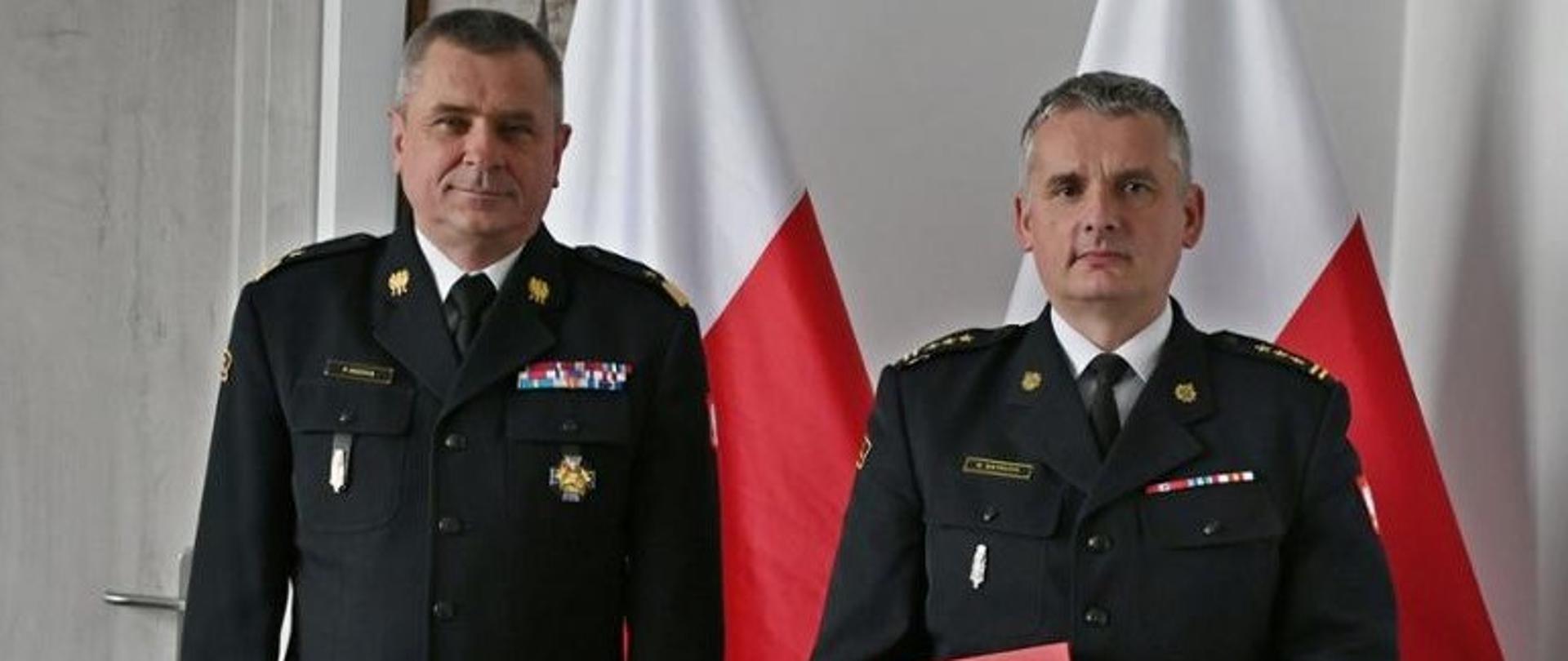 Pomorski Komendant Wojewódzki Państwowej Straży Pożarnej nadbryg. Piotr Socha stoi w towarzystwie powołanego na stanowisko Komendanta
Powiatowego Państwowej Straży Pożarnej w Człuchowie st.bryg Radosława Batruch. W tle dwie flagi państwowe.