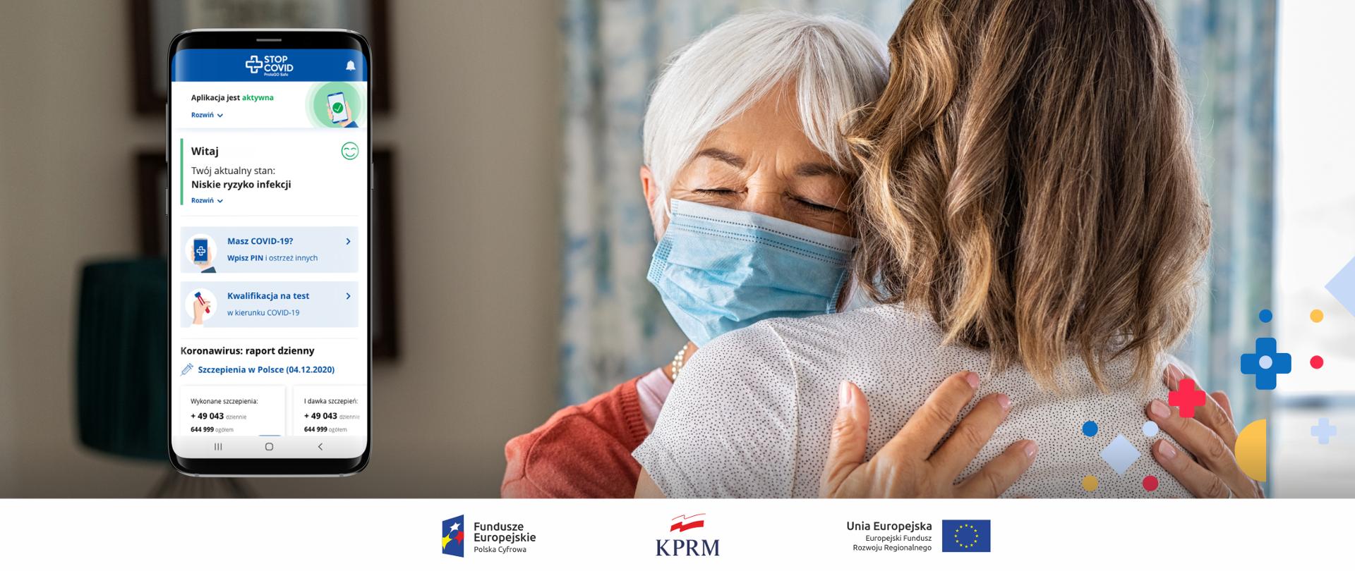 Dwie obejmujące się kobiety - matka i córka. Z przodu widoczna starsza z nich, ubrana w maseczkę. Młodsza - widoczna tyłem. Z lewej strony - grafika przedstawiająca ekran smartfona, na którym wyświetla się aplikacja STOP COVID.
