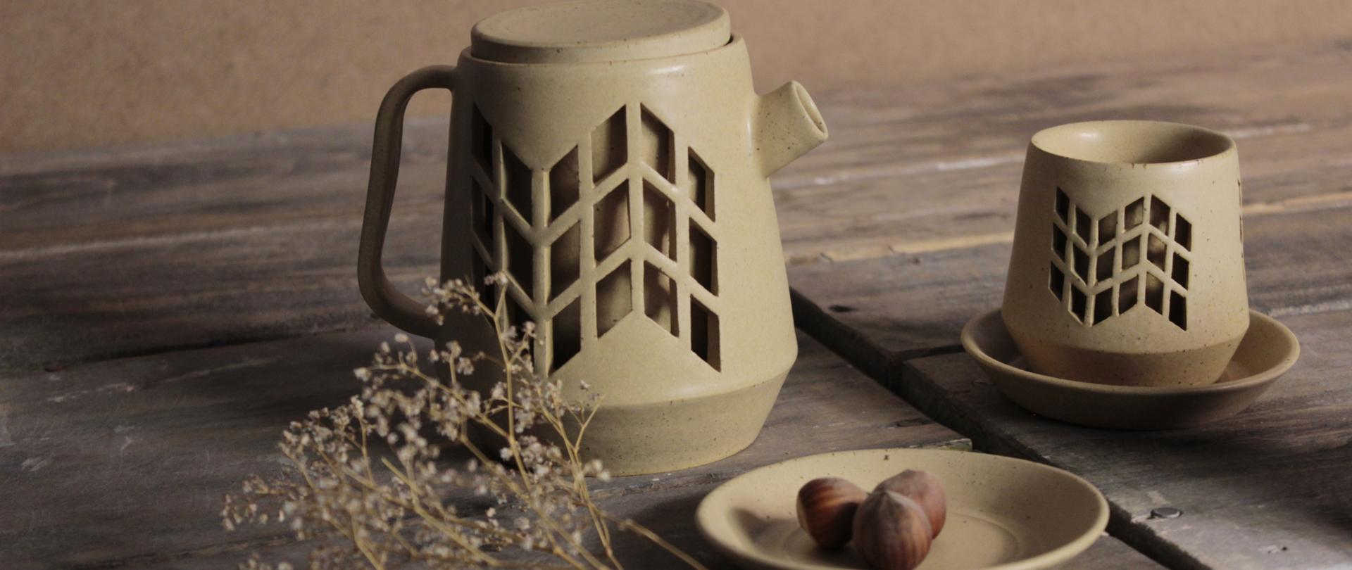 Zdjęcie: na deskach ceramiczny dzbanek, filiżanka i talerzyk na którym leżą trzy orzechy laskowe.