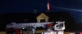 Na zdjęciu widać płomienie ognia wychodzące z komina domu jednorodzinnego oraz strażaków prowadzących akcję gaśniczą.
