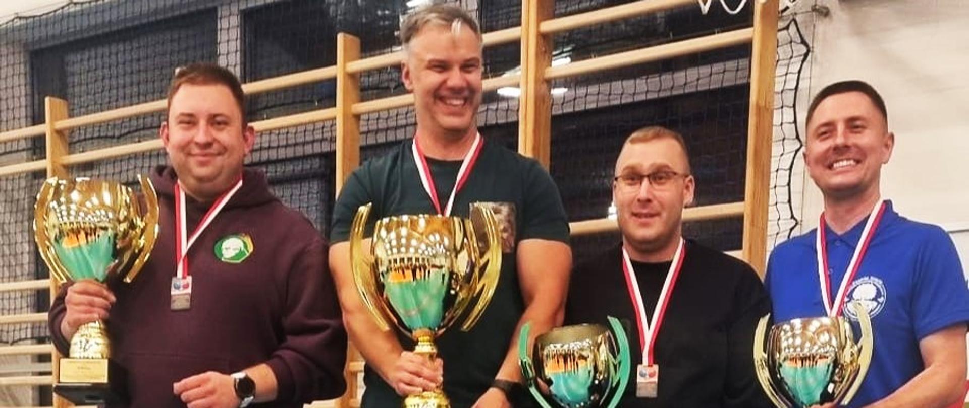 Czterej mężczyźni z pucharami w rękach i medalami na szyi.