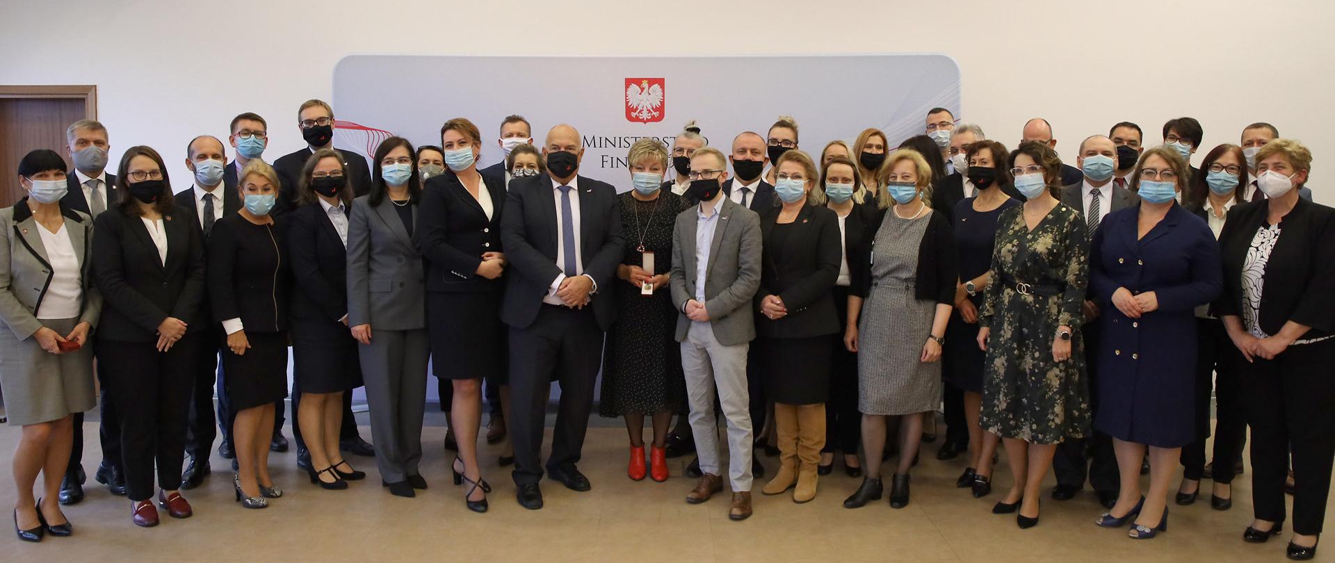 Minister Tadeusz Kościński i wyróżnione osoby na tle banera MF 