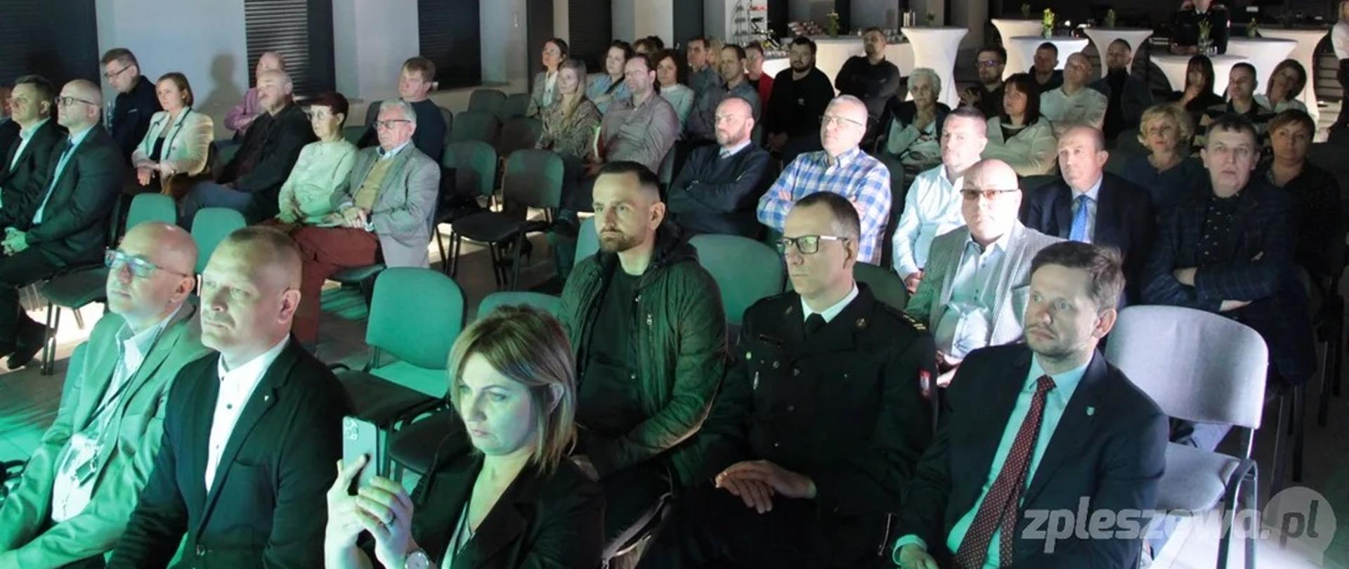 Grupa kobiet i mężczyzn siedzi w zaciemnionym pomieszczeniu widowiskowym.