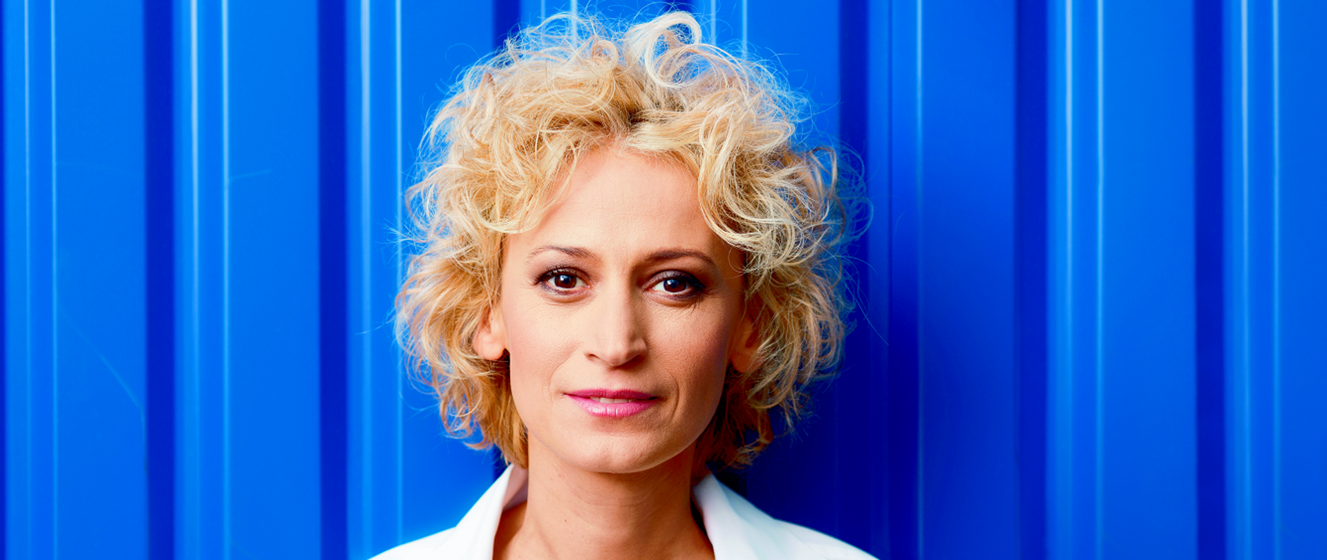 Na niebieskim tle ubrana w białą koszulę o blond włosach kobieta