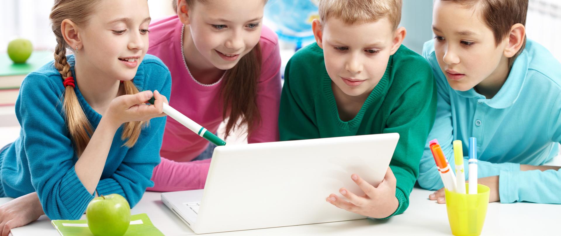 Weseli uczniowie patrzą na laptopa w klasie