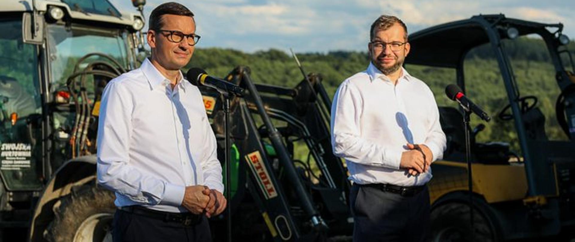 Premier Mateusz Morawiecki oraz minister rolnictwa Grzegorz Puda na tle ciągników i maszyn rolniczych