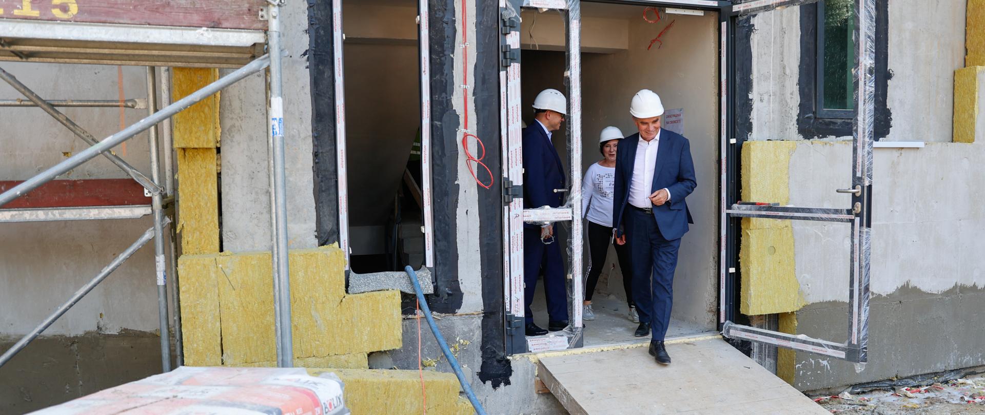 Wojewoda lubelski w białym kasku wychodzi z budynku w budowie. 