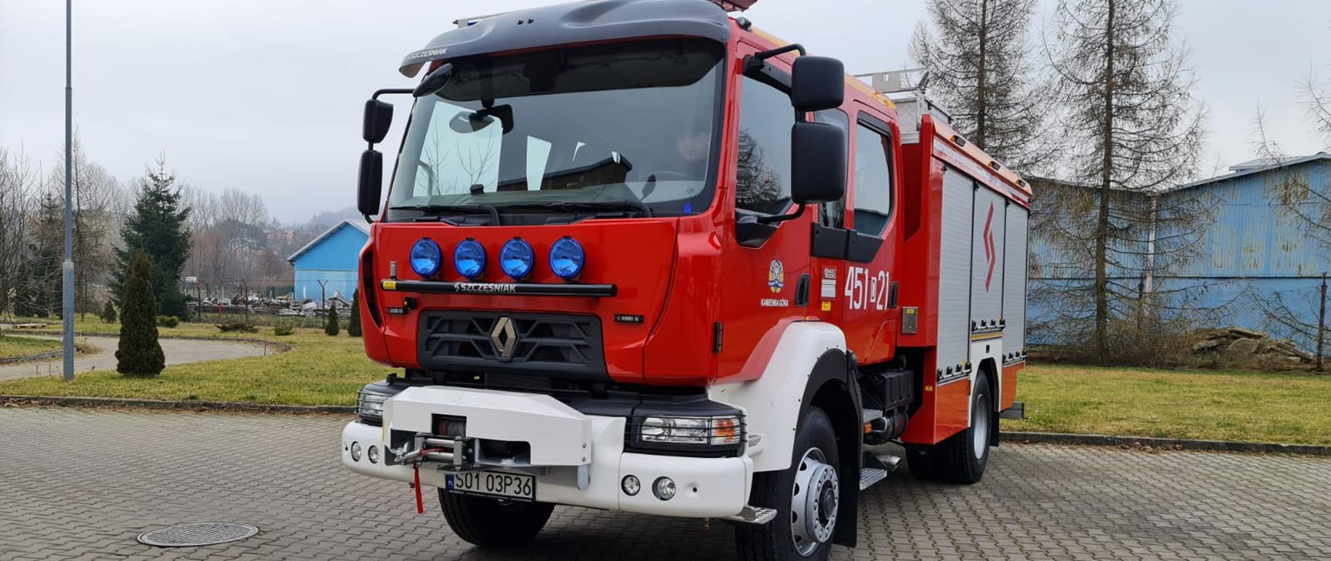 Samochód ratowniczo gaśniczy , zdjęcie przedstawia ustawiony pojazd lekko skierowany do prawego boku widać lewy bok samochodu marki renault stojący na parkingu w tle trawa