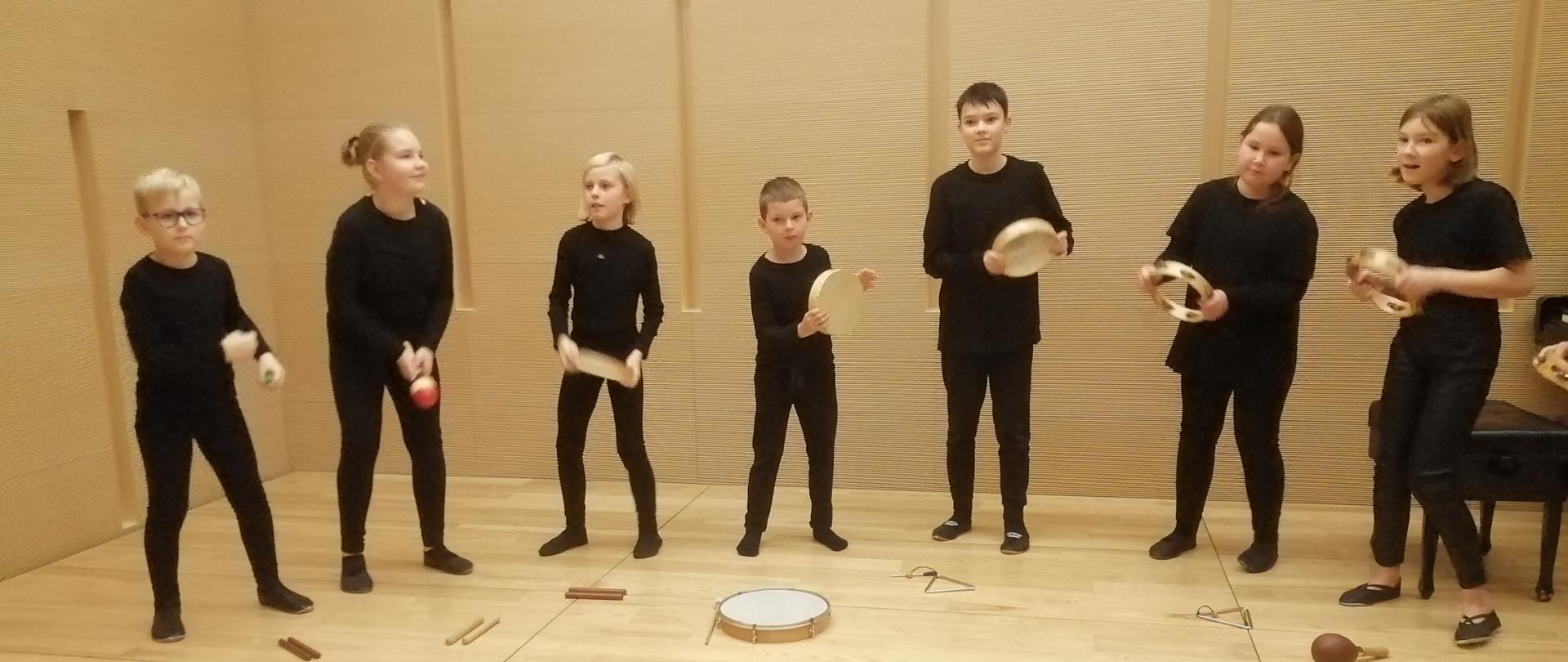 Na scenie występują grupa uczniów. Wszyscy są ubrani na czarno. W rękach trzymają instrumenty