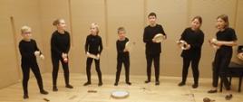 Na scenie występują grupa uczniów. Wszyscy są ubrani na czarno. W rękach trzymają instrumenty