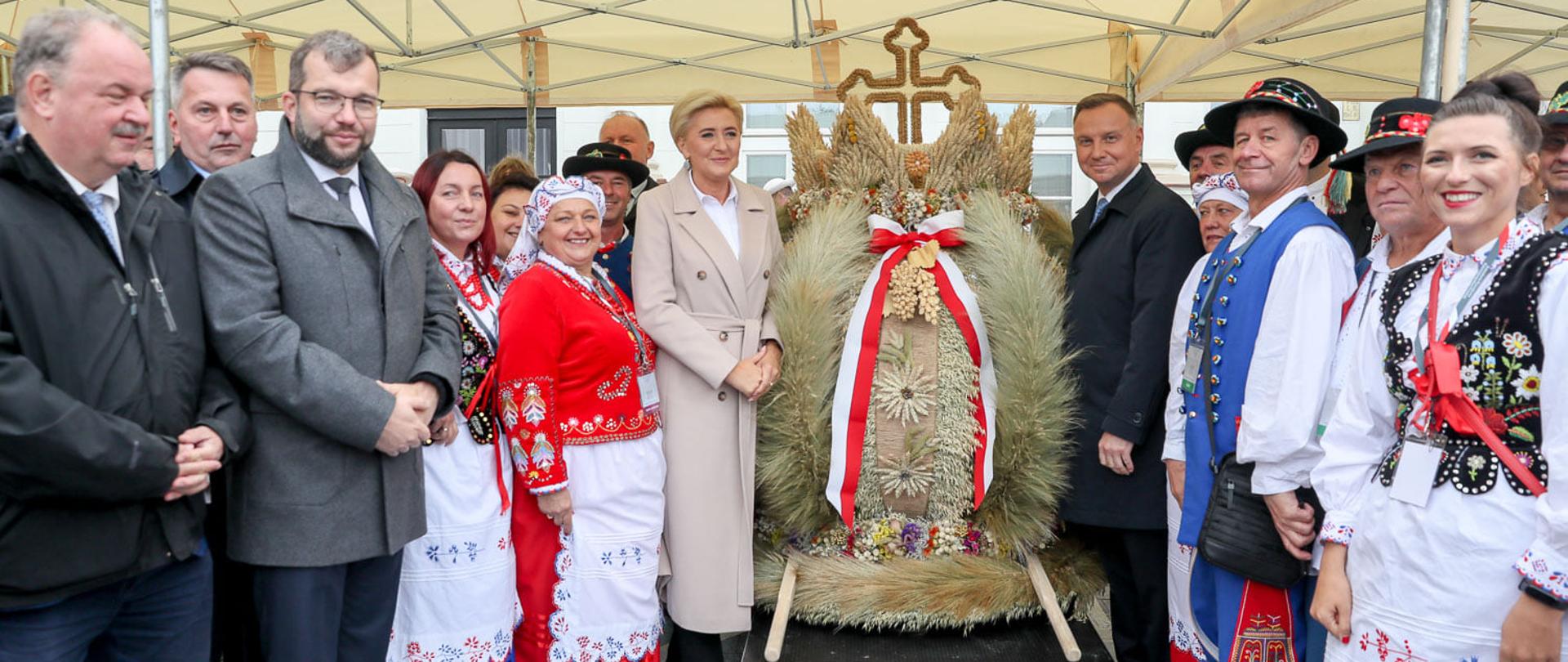 Prezydent RP Andrzej Duda wraz z Pierwszą damą i ministrem rolnictwa i rozwoju wsi Grzegorzem Pudą stojący przy dożynkowym wieńcu.