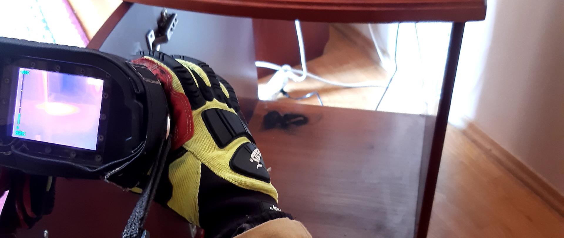 Strażak sprawdza kamerą termowizyjną temperaturę szafki. 